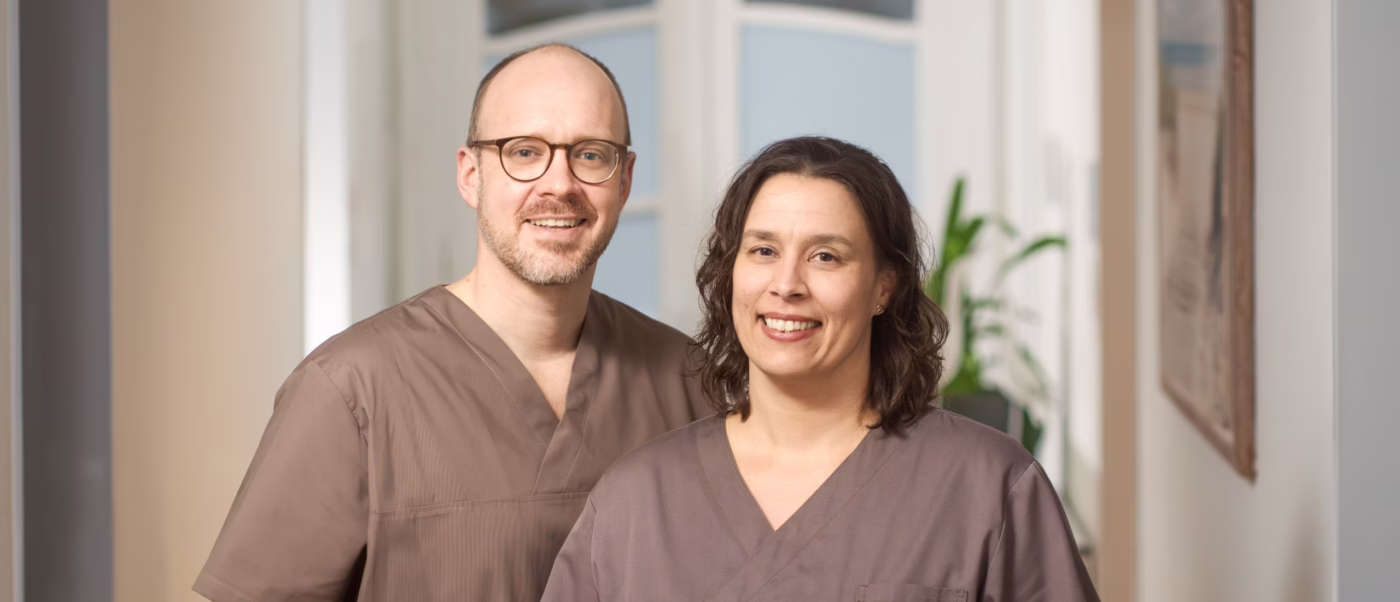 Zwei Ärzte stehen im Praxisflur und lächeln in die Kamera